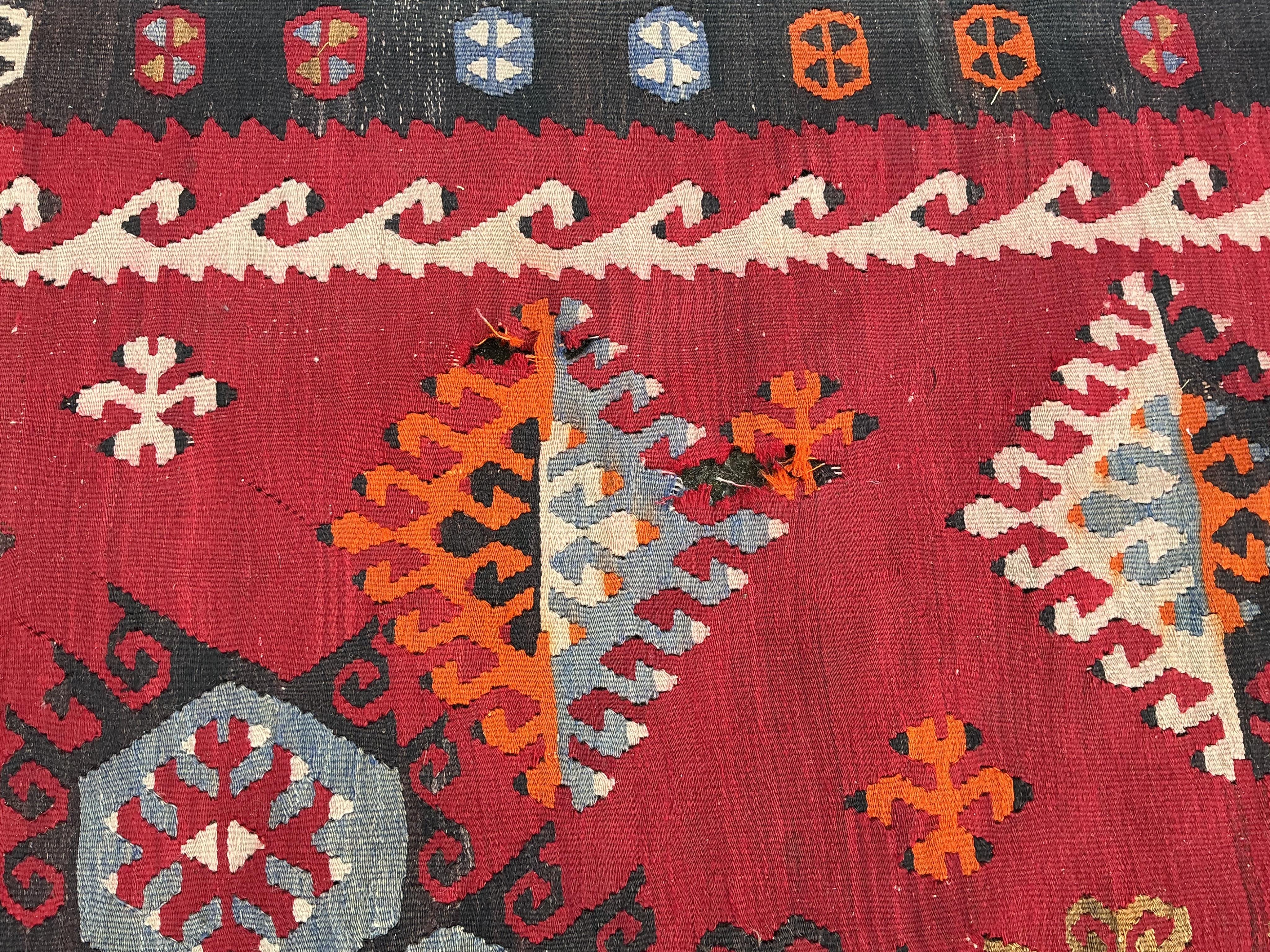 A Turkish Anatolian polychrome flatweave Kilim carpet, woven with geometric lozenges on a red field, 367 x 292cm